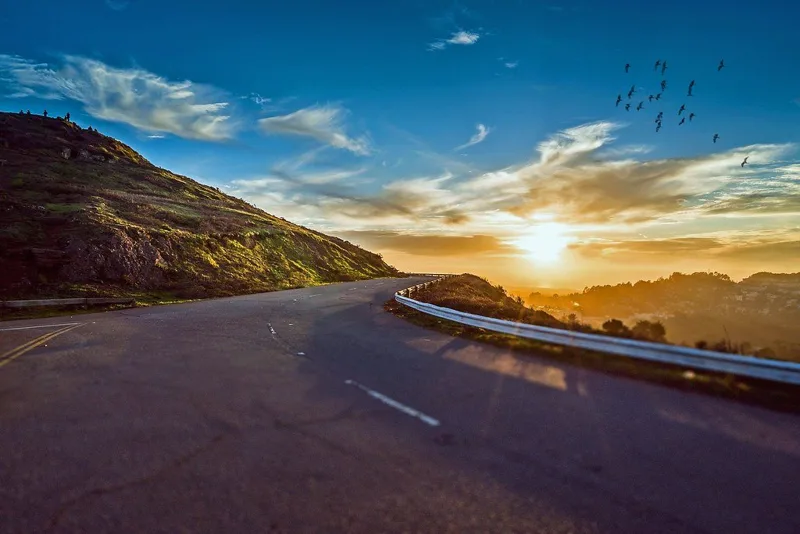 夕日に向かって山あいを曲がりながら続く道路の写真