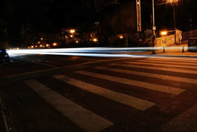 夜の横断歩道を横切る車のライトの軌跡の写真